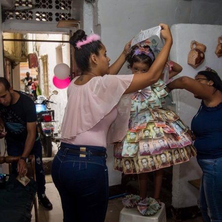 Jesay Ramirez ajusta el disfraz de su hija Nazareth Yanez, confeccionado de forma artesanal por su familia con billetes de Bolívares Foto EFE