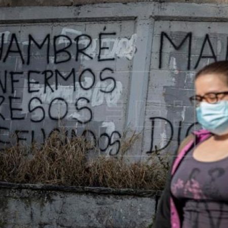 Una mujer camina frente a una pared con un graffiti pintado que dice "Hambre, enfermos, presos, refugiados". ( Foto Referencial)