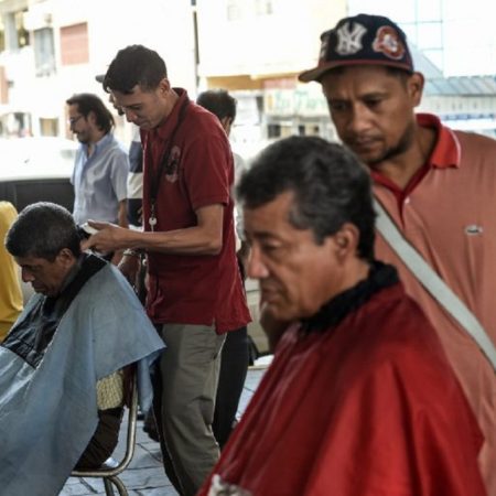 Two men work cutting hair under a bridge in Caracas on May 28, 2018.
Under a bridge or in an open-air market in Caracas, hairdressers make their living with simple tools and offer cheeper haircuts to those who can not afford a beauty salon because of the economic crisis. / AFP PHOTO / Juan BARRETO